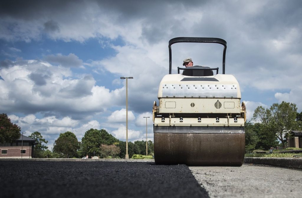 Road workers laying fresh asphalt during a road resurfacing project with machinery nearby.